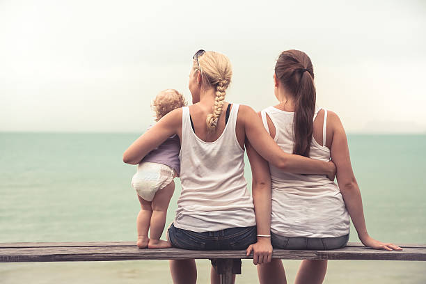 Loving mother embracing her children looking into the distance Loving mother embracing her children sitting on wooden bench at tropical beach during vacation. They together looking into the distance. Concept for togetherness and  bright future behavior femininity outdoors horizontal stock pictures, royalty-free photos & images