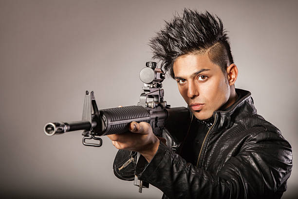 Young middle eastern man with black leather jacket in black suit holding gun. studio shot.