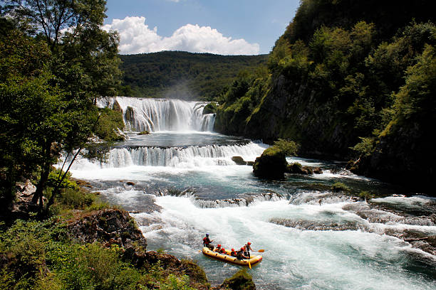 Near city of Bihac, Bosnia and Herzegovina - July 20, 2016: River Una, unique beauty in Europe and group of tourists in rubber raft. With professional skipper it is easy to relax and to enjoy in nature, rapids and cascades.