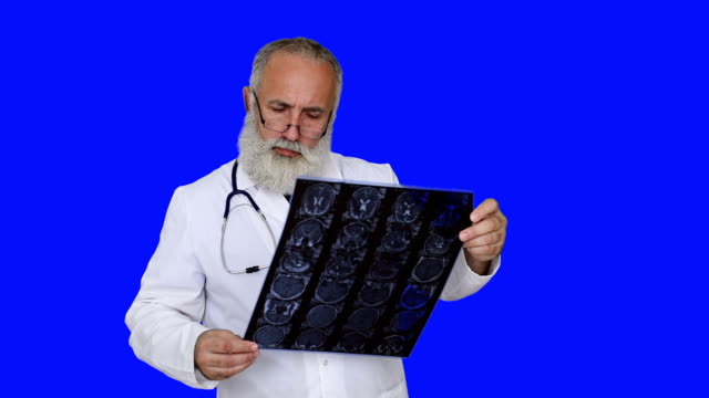 adult senior doctor looks picture MRI of the head on a blue background