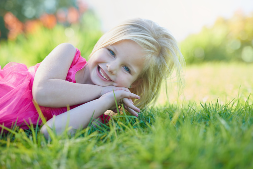a 5-6-year-old girl lies in the Park on the grass and laughs, happy childhood, child's day.