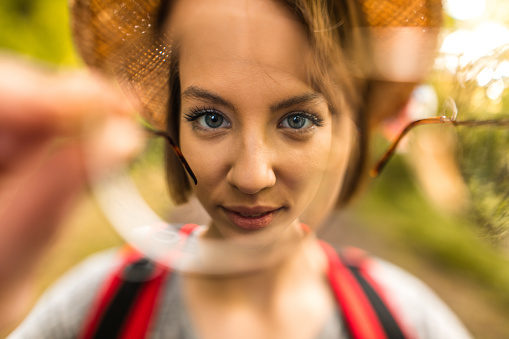 Close up of young woman seen through eyeglasses lens in nature.