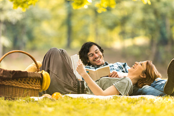 Happy couple laughing while reading book at picnic.