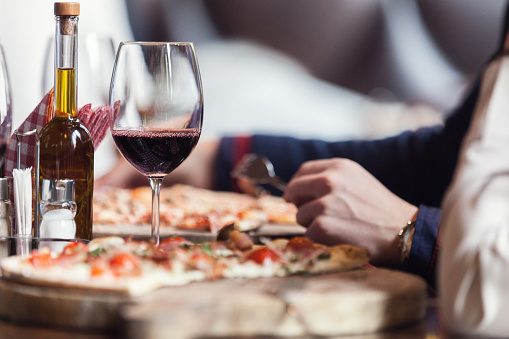 Unrecognizable man eating pizza in restaurant, focus on red wine