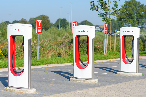 Zwolle, The Netherlands - August 19, 2016: Tesla electric car supercharger charging station with green trees in the background. Superchargers are free connectors that charge Model S in minutes. Superchargers are used for long distance travel, located along the most popular routes in North America, Europe and Asia.