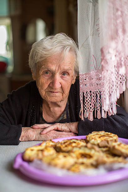istock Elderly woman sits at a table with a rustic pastries. 611769158