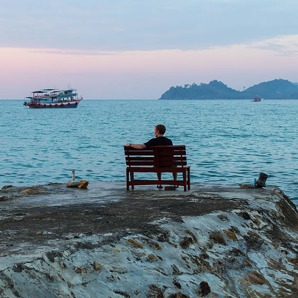 istock Lonely man sitting on a bench looking at the sea 611779834
