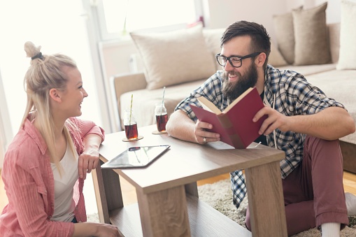 Couple of students sitting on the floor in the living room, discussing exam materials. Focus on the guy, lens flare effect on the window