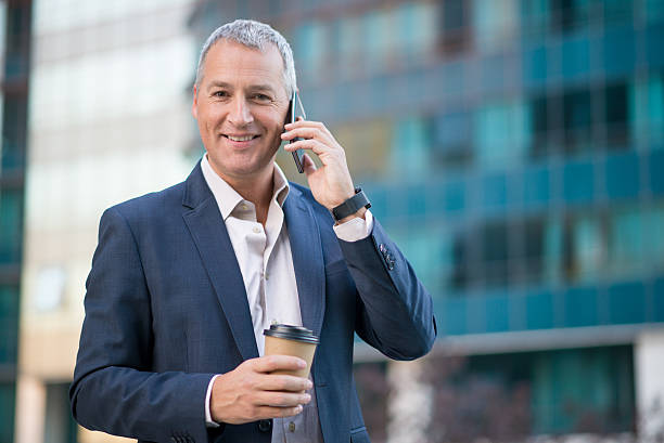 istock businessman using smartphone  and holding coffee to go outside 611785692