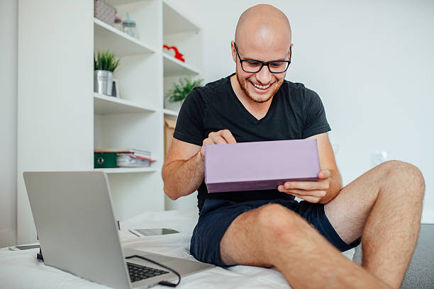 Young man enjoyng opening box and sitting on the bed. stock photo