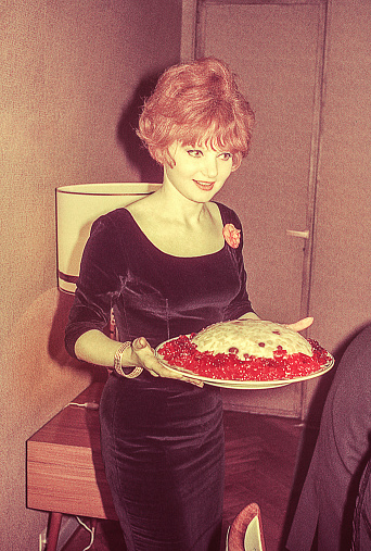 Vintage photo from the sixties, featuring a beautiful young woman serving food at a dinner party event