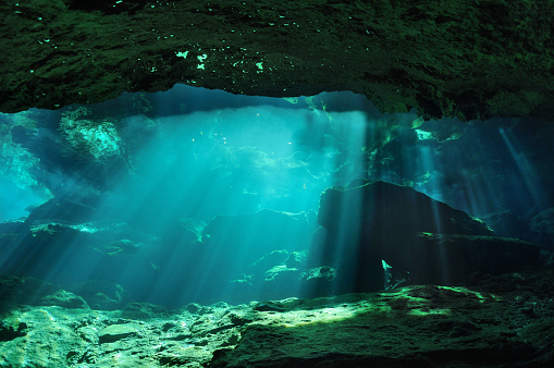 Sunbeams penetrate through the waters of Chac mool cave producing mysterious reflections on the surface in the background, Yucatan peninsula, Mexico