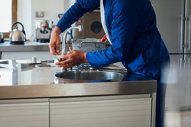 Repairman at Work A shot of a man's hands working on a kitchen sink. He is wearing blue overalls with his tool kit in the background. adjusting stock pictures, royalty-free photos & images
