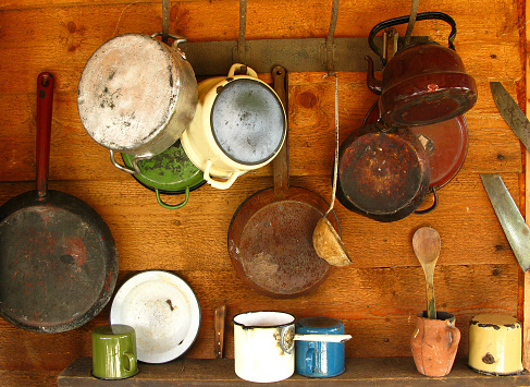 Scratched and damaged old frying pans and cooking pots hanging on a wooden wall