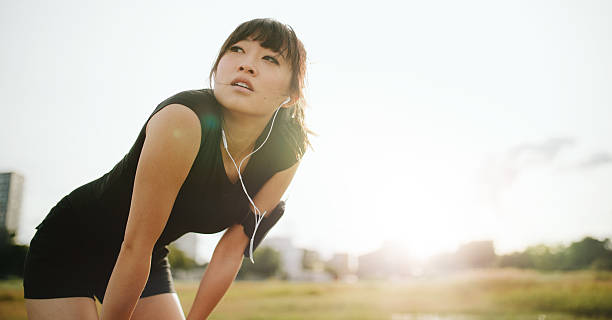 Young athletic woman taking a break from training Young athletic woman taking a break from training. Chinese female standing with hands on her knees and looking away in morning. determination asian stock pictures, royalty-free photos & images