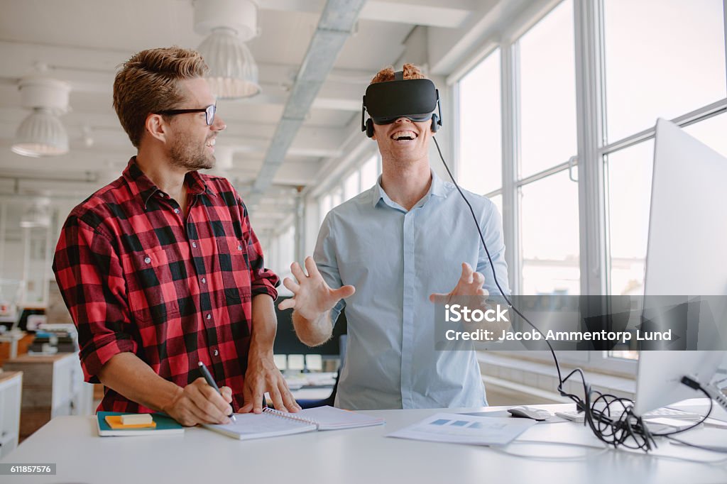 Young developers testing new virtual reality device Shot of two young men testing virtual reality glasses in office. Businessman wearing VR goggles and colleague writing notes. Leisure Games Stock Photo