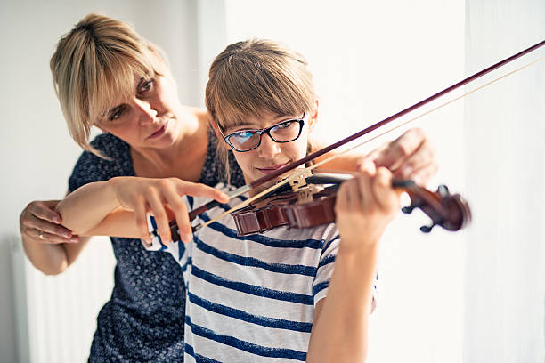 Teenage girl violin lesson Teenage girl aged 10 is practicing violin. Mother is helping her by correcting her posture. Both are having fun during the lesson.  violinist photos stock pictures, royalty-free photos & images