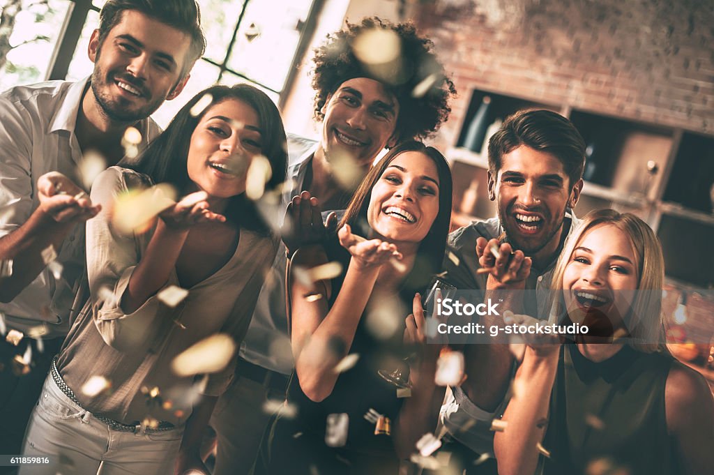 Confetti fun. Cheerful young people blowing confetti and smiling while enjoying party together Happiness Stock Photo