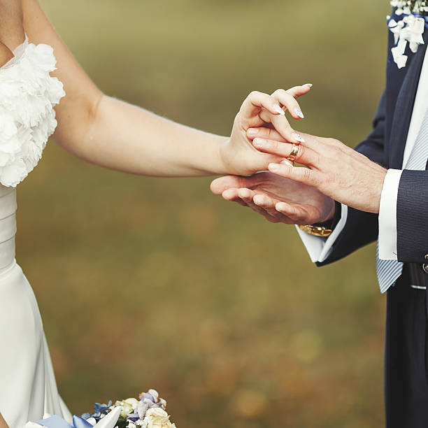 istock putitng golden ring to brides finger 611861236