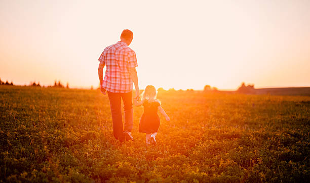 istock Dad and daughter walking in field at sunset 611875960