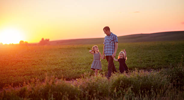 istock Dad and daughter walking in field at sunset 611876174