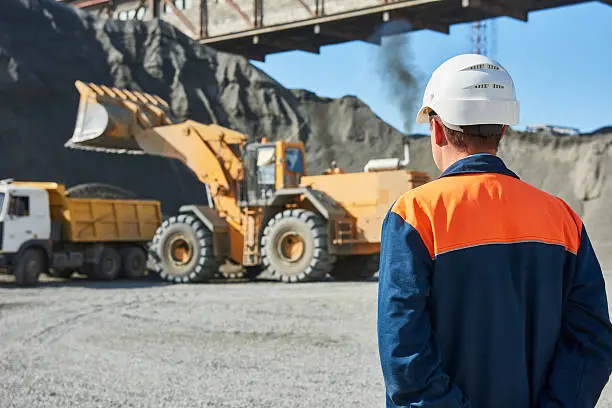Mining industry. Construction worker engineer supervisor looking at heavy wheel loader loading granite rock or ore into dumper truck