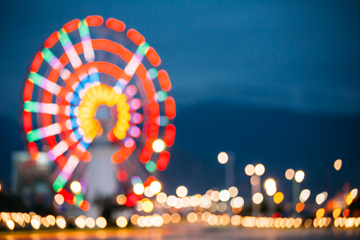 Abstract Motion Blur Image Of Brightly Colorful Illuminated Ferris Wheel In Amusement City Park On Black Blue Evening Sky Bokeh Boke Background.