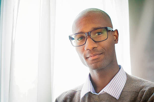 hermoso retrato intelectual calvo negro maduro por ventana - cardigan men african ethnicity african descent fotografías e imágenes de stock