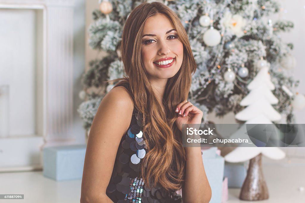 Fashion woman is sitting near christmas tree Happy smiling pretty girl is sitting infront of fireplace and christmas tree, new year time Christmas Stock Photo