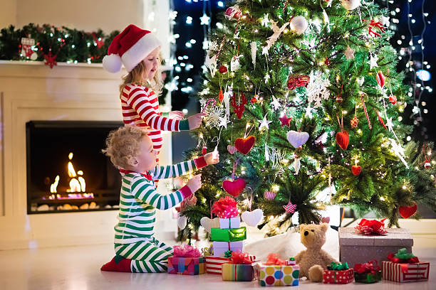 istock Kids decorating Christmas tree in living room with fire place 611890410