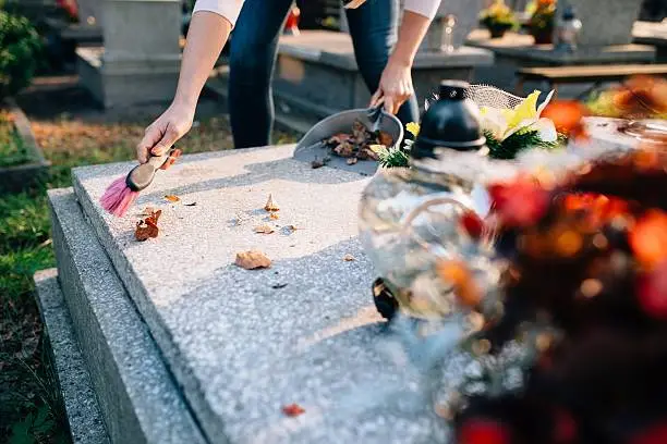 A woman cleans the grave. Sweeps leaves from the tombstone. Preparations for All Saints Day on November 1