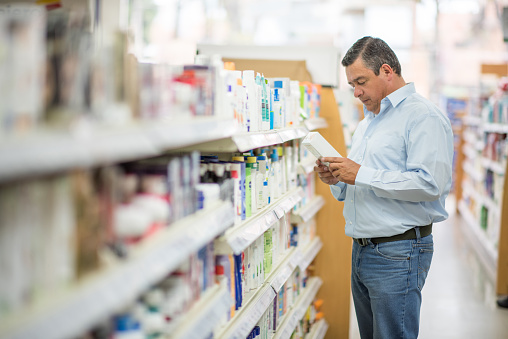 Happy Latin American man shopping at the pharmacy and holding a product