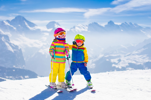 Kids skiing in mountains. Active children with safety helmet, goggles and poles. Ski race for young kids. Winter sport for family. Child ski lesson in alpine school. Little skier racing in snow