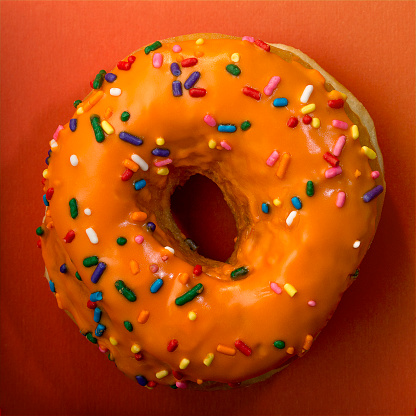 Close image of a  frosted donut with multicolored sprinkles. Images is croped to 1:1 square