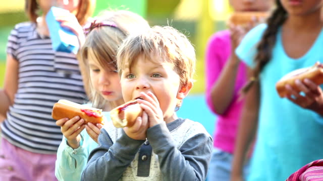 Little boy and group of children eating hotdogs