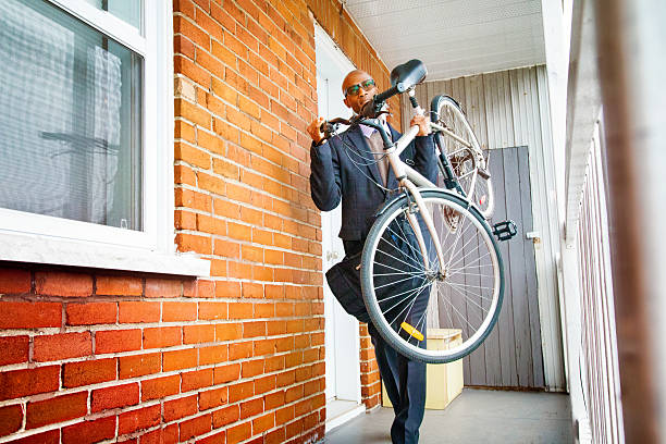 Businessman lifting bicycle up as he leaves his apartment for work and prepares to descend stairways.