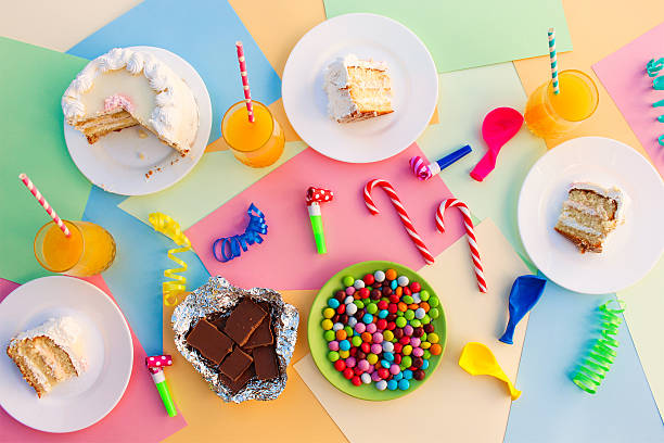 Cake, candy, chocolate, whistles, streamers, balloons, juice on holiday table.