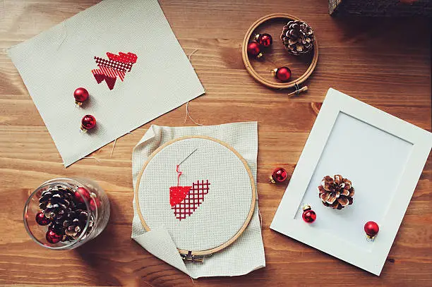 Christmas cross stitch designs and decorations on wooden table. Preparing handmade gifts for New Year and Christmas at homeChristmas cross stitch designs and decorations on wooden table. Preparing handmade gifts for New Year and Christmas at home