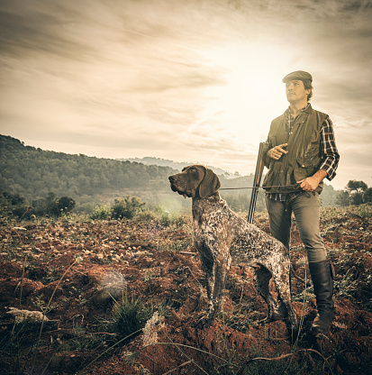 Hunter with German Shorthaired pointer in abandoned field during the morning