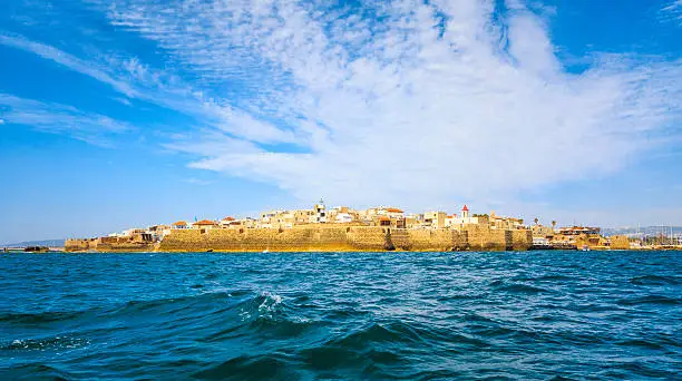 View from the sea to the ancient fortress city of Acre in Israel against the backdrop of a colorful sky.