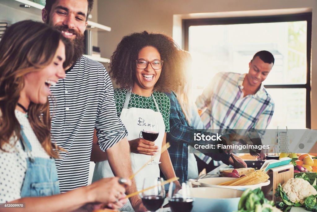 Group of diverse friends drinking and cooking Group of diverse friends drinking and cooking in front of long food preparation table indoors Cooking Stock Photo
