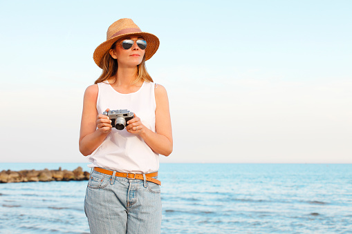 Portrait of a middle age woman standing on the beach while on summer vacation and taking pictures with her vintage camera.