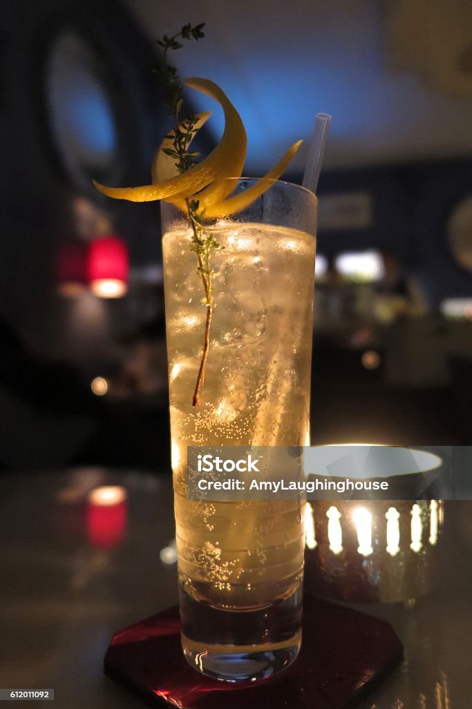 highball cocktail with lemon twist and thyme highball cocktail garnished with lemon twist and a sprig of thyme backlit by a candle, illuminating bubbles in the glass Lemon - Fruit Stock Photo