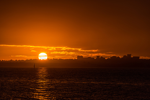 Orange hues of tropical sunset over water with cityscape silhoue