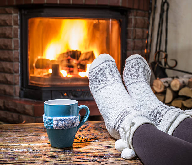 Relaxing near fireplace with a cup of hot drink. Warming and relaxing near fireplace. Woman feet near the cup of hot drink in front of fire. heat home interior comfortable human foot stock pictures, royalty-free photos & images