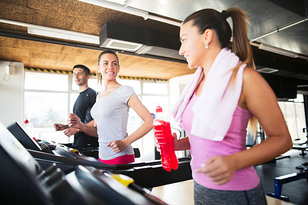 istock Young woman holding refreshment drink while exercising on treadmill. 612016348