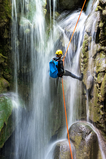 Canyoneering member with backpack rappeling down the waterfall in the canyon.
