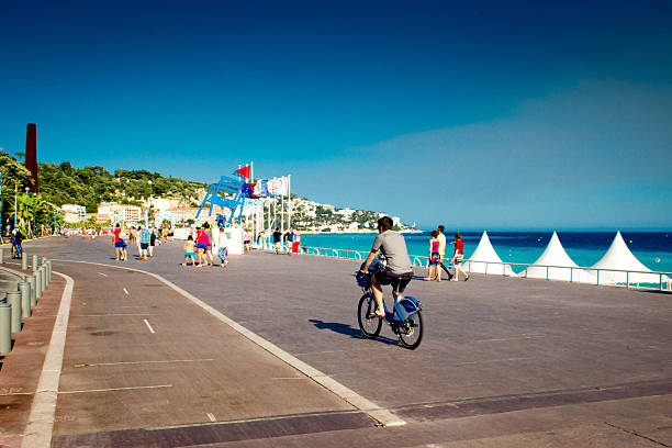Nice, France - July 29, 2015: Cyclist riding his bicycle along the promenade in front of the beach in Nice, France. This has a polarized blue sky.