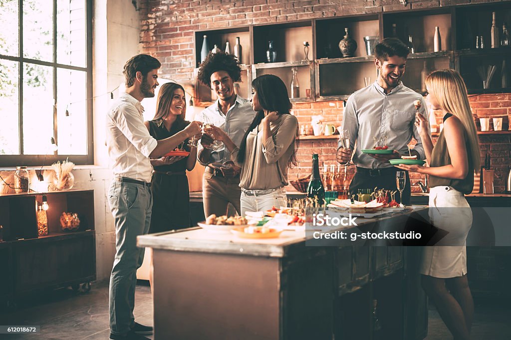 Enjoying party with nearest friends. Group of cheerful young people enjoying home party with snacks and drinks while communicating on the kitchen Party - Social Event Stock Photo