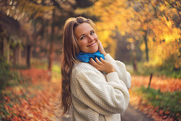 Young women smiling to the camera, beautiful autumn road in the background.